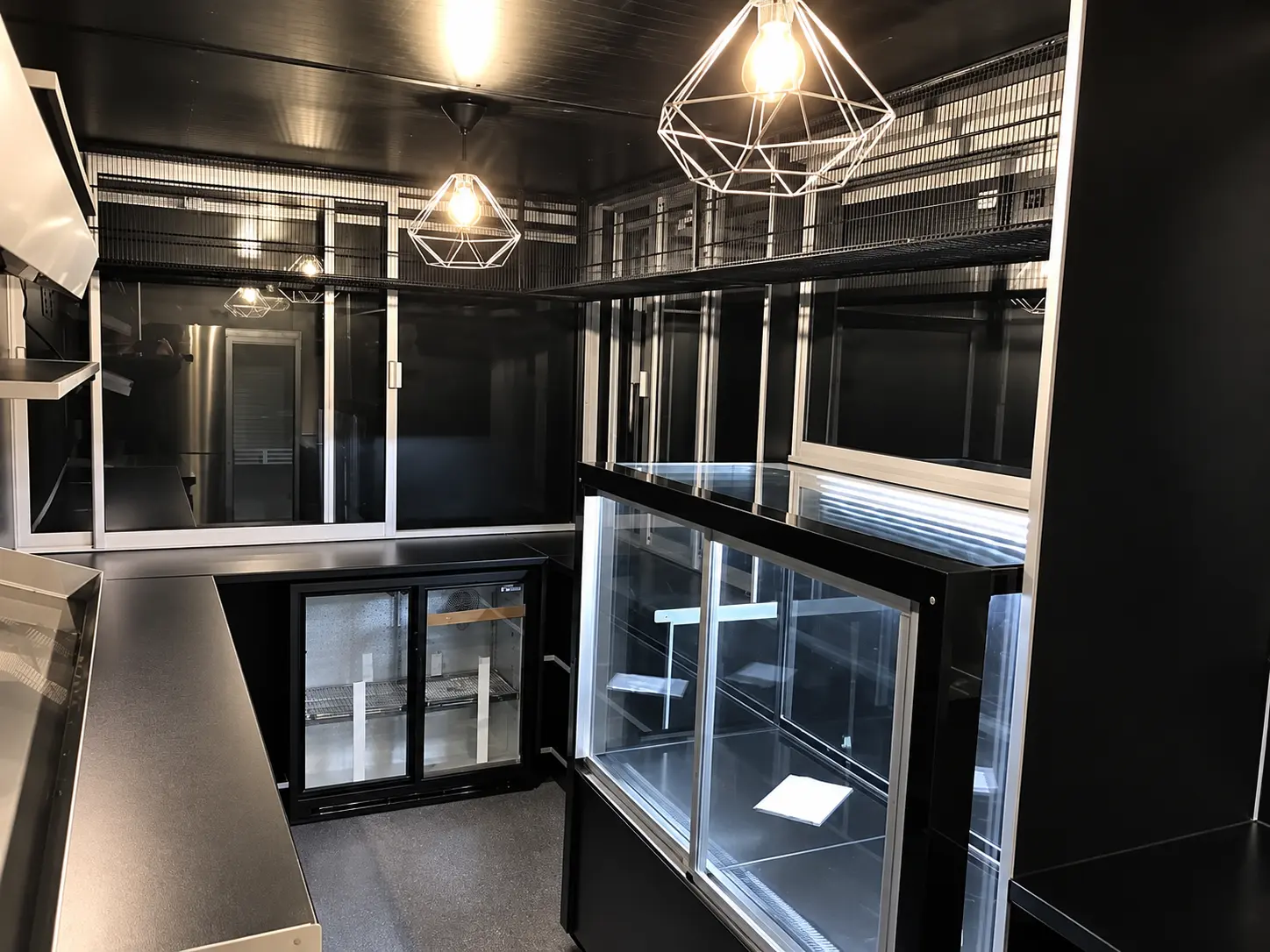 Dark interior of a portable food kiosk with glass display counter, under-counter fridge and geometric pendant lights