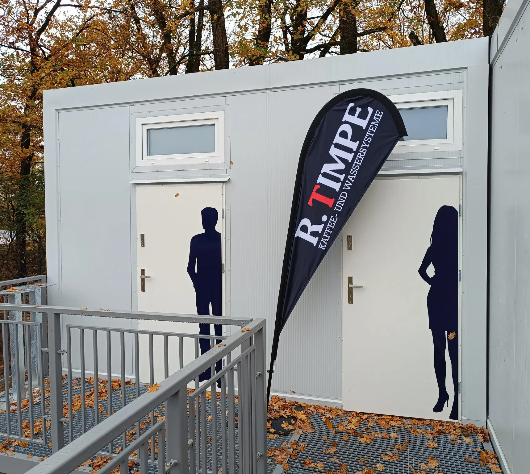 White portable twin toilet unit with separate male and female door graphics and an external access ramp