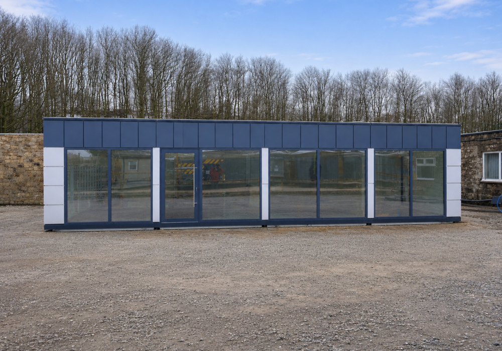Dark blue and white modular building with full-height glazed sliding door frontage on a gravel site