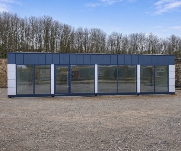 Exterior of a navy blue modular building with white pilasters and full-height glazed frontage on a gravel yard