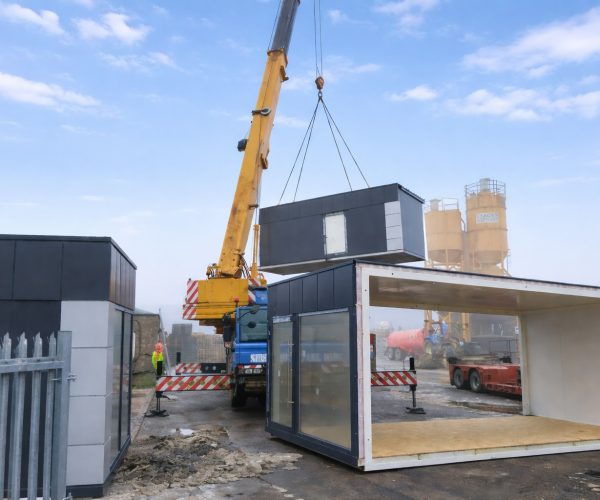 Mobile crane lifting a modular building module into place during on-site installation at an industrial yard