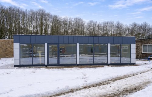 Navy blue modular building with a glazed frontage standing in a snow-covered yard in winter