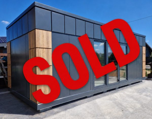 Dark grey modular building with timber-effect accent cladding and glazed doors, marked with a red Sold overlay