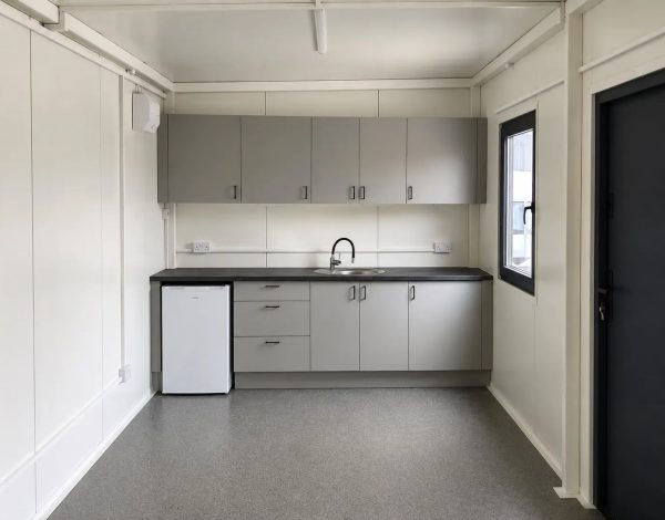 Interior of portable cabin with grey fitted kitchen units dark worktop sink and under-counter fridge