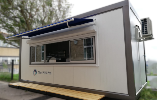 White portable school kiosk pod branded The 1926 Pod with blue retractable awning and timber deck step outside school