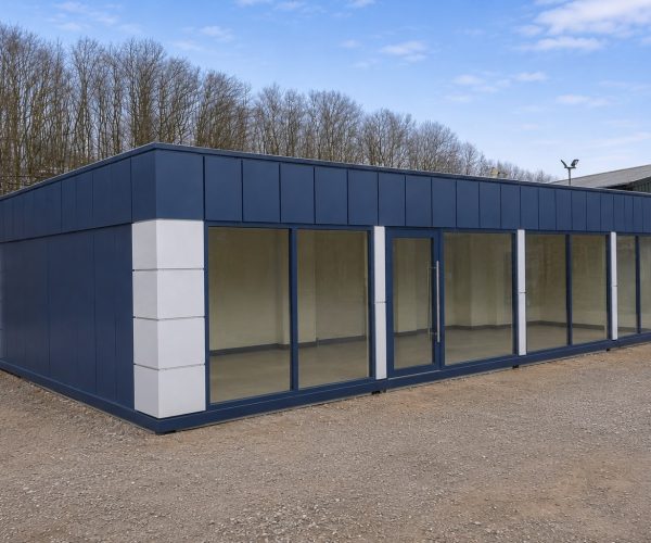 Exterior of an anthracite modular building with silver pilasters and full-height glazed frontage on a gravel yard